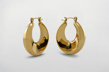 Load image into Gallery viewer, A pair of gold Dynasty Hoops with a sleek, minimalist hollow design, crafted from stainless steel with luxurious PVD gold plating. These water-resistant hoops, engraved with a signature submark logo, symbolize timeless elegance and strength. Perfect for everyday wear or statement styling, they honor the legacy of bold, stylish women across generations.
