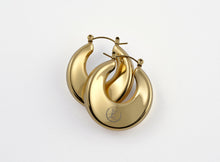 Load image into Gallery viewer, A pair of gold Dynasty Hoops with a sleek, minimalist hollow design, crafted from stainless steel with luxurious PVD gold plating. These water-resistant hoops, engraved with a signature submark logo, symbolize timeless elegance and strength. Perfect for everyday wear or statement styling, they honor the legacy of bold, stylish women across generations.