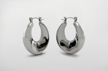 Load image into Gallery viewer, A pair of silver Dynasty Hoops with a sleek, minimalist hollow design, crafted from stainless steel with luxurious PVD gold plating. These water-resistant hoops, engraved with a signature submark logo, symbolize timeless elegance and strength. Perfect for everyday wear or statement styling, they honor the legacy of bold, stylish women across generations.
