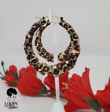 Load image into Gallery viewer, The picture is of a pair of bamboo earrings made from lightweight iron alloy material. They are in a circular hoop shape and have a leopard print design on them. The earrings have a gold-toned metal stem that goes through the earlobe.