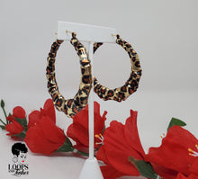 Load image into Gallery viewer, The picture is of a pair of bamboo earrings made from lightweight iron alloy material. They are in a circular hoop shape and have a leopard print design on them. The earrings have a gold-toned metal stem that goes through the earlobe.