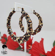 Load image into Gallery viewer, The picture is of a pair of bamboo earrings made from lightweight iron alloy material. They are in a circular hoop shape and have a leopard print design on them. The earrings have a gold-toned metal stem that goes through the earlobe.