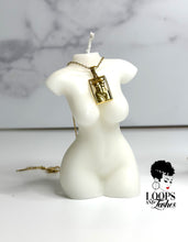 Load image into Gallery viewer, A gold masterpiece necklace resting on a candle shaped like a women&#39;s body, symbolizing body positivity and empowerment
