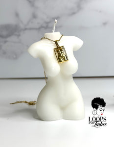 A gold masterpiece necklace resting on a candle shaped like a women's body, symbolizing body positivity and empowerment