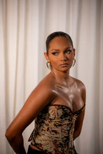 Load image into Gallery viewer, Woman wearing Loops and Lashes® Zen Stud earrings with a sleek updo and patterned corset top, showcasing minimalist gold geometric stud design.
