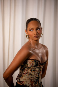 Woman wearing Loops and Lashes® Zen Stud earrings with a sleek updo and patterned corset top, showcasing minimalist gold geometric stud design.