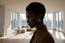 Load image into Gallery viewer, Woman wearing gold hoop earrings with a plain background
