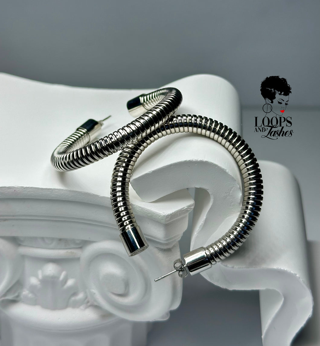 A pair of Heritage Hoops in sleek silver, crafted from high-quality stainless steel with a durable PVD plating. These two-inch open hoop earrings feature a unique textured design and an exclusive engraved submark logo, symbolizing timeless elegance and empowerment. Waterproof and tarnish-resistant, they blend modern sophistication with lasting quality.