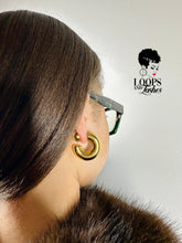 Load image into Gallery viewer, Close-up of a person wearing gold hoop earrings with 'Loops and Lashes' logo in the corner.
