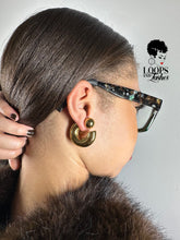 Load image into Gallery viewer, Close-up of a person wearing gold hoop earrings with a neutral background

